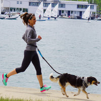 Mujer corriendo junto al mar con su perro y la correa en la cintura
